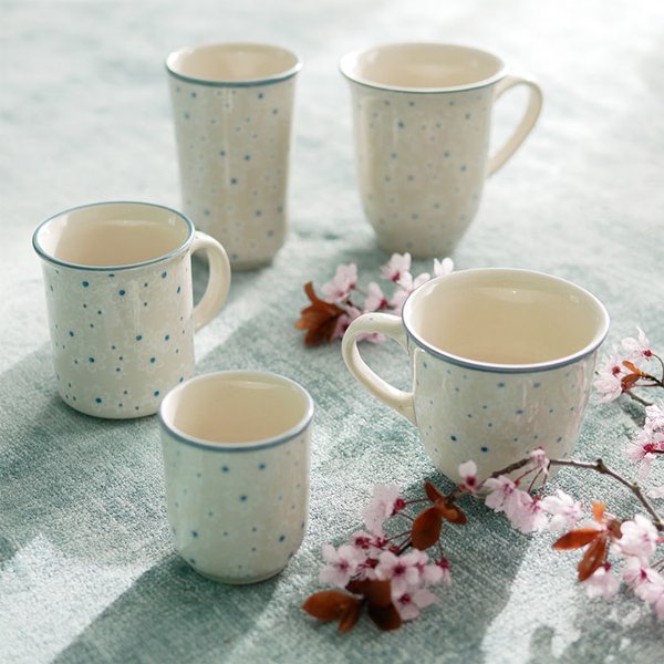 Bunzlauer Keramik Tassen in hellem Dekor (weiß-blaue Blüten) und diversen Formen auf gedecktem Tisch